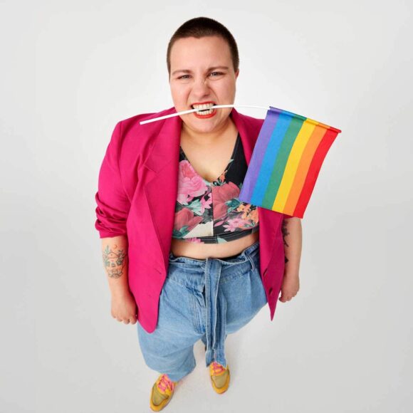 Kobieta w kolorowym stroju z tęczową flagą w zębach