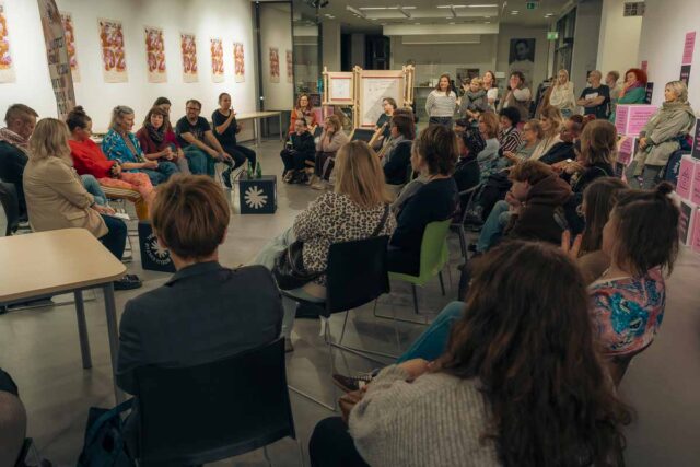 ludzie siedzą na krzesłach we foyer przed nimi kilka osób rozmówców przodem