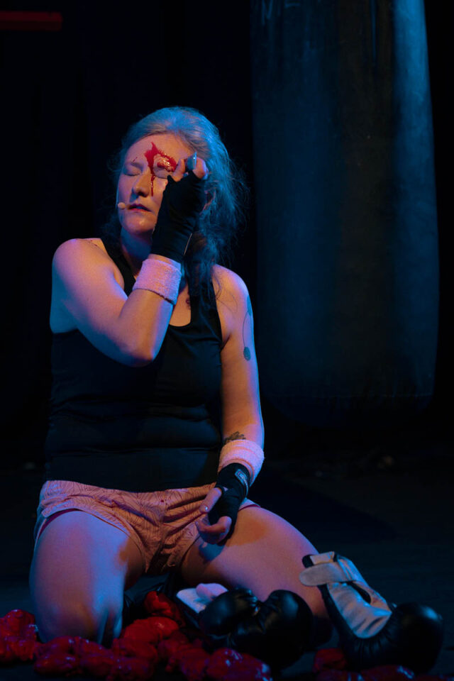 Kobieta w sportowym stroju siedzi na podłodze, maluje twarz farbą jakby krwią