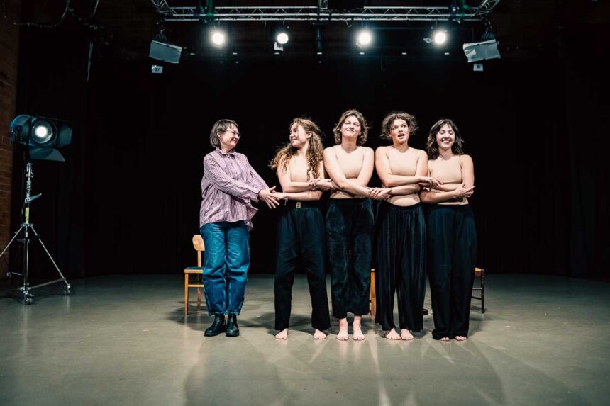 Cztery młode kobiety w cielistych topach trzymające się za ręce, obok nich reżyserka w koszuli i jeansach