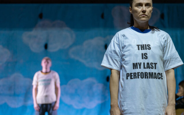 Kobieta w białym t-shircie z napisem: this is my last performance, w tle męzczyzna