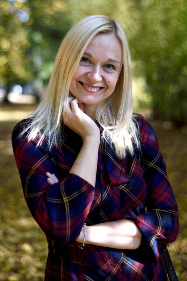 Izabella Adamczewska - kobieta w sukience, z blond włosami na tle zieleni