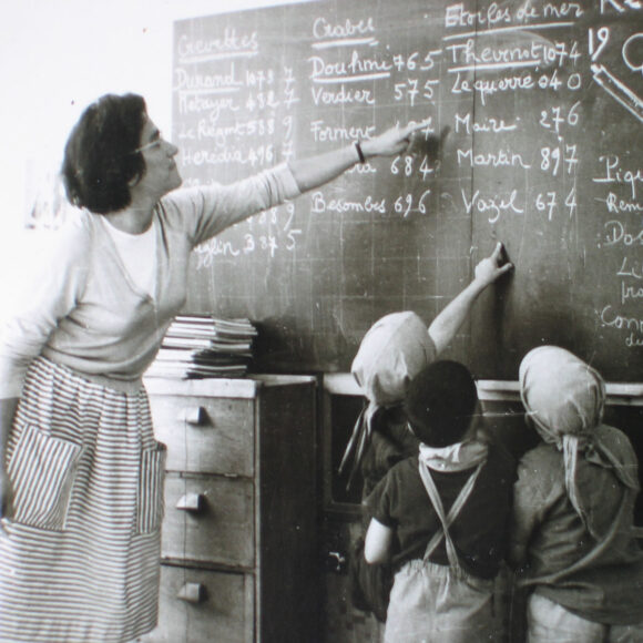 Kobieta z trójka dzieci przy tablicy w szkole, zdjęcie archiwalne