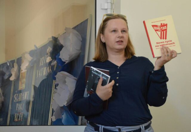 Kobieta w ciemnej bluzce trzyma w rękach dwie ksiązki