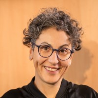 Kobieta w krótkich kręconych włosach, okularach uśmiecha się