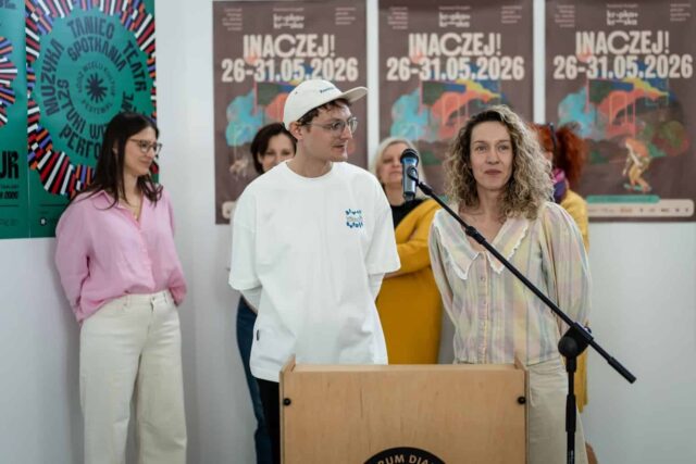 Kobieta i meżczyzna na tle plakatów stoją przy mikrofonie w trakcie konferencji