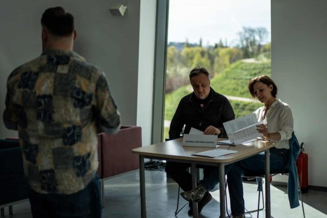 Kobieta i mężczyzna siedzą przy stole na tle okna, na pierwszym planie mężczyzna w kolorowej koszuli tyłem