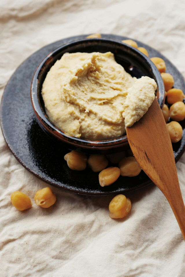 hummus w czarnej misce, ziarna ciecierzycy dookoła