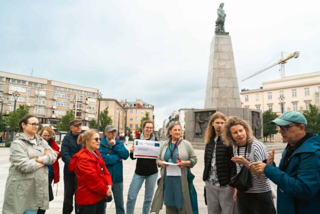 Grupa kilkunastu osób - uczestników spaceru stoi przodem w tle pomnik Kościuszki