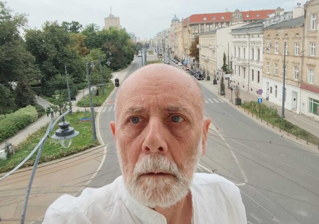 Portret starszego mężczyzny w białej koszuli na tle panoramy miasta