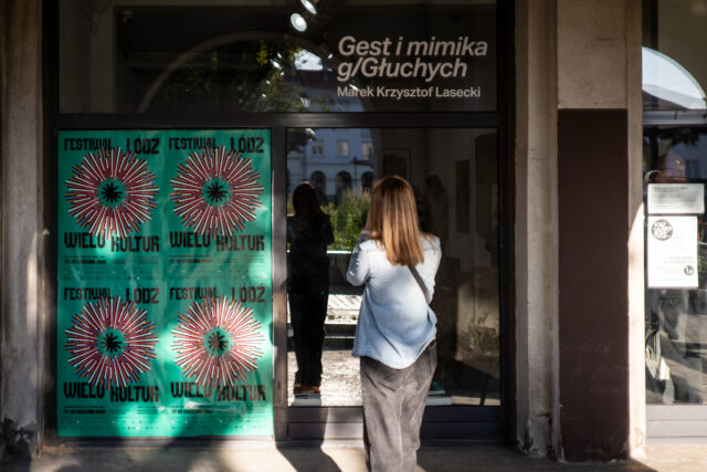 Kobieta tyłem - fotografuej wejście do Galerii z plakatami Festiwal Łódź Wielu Kultur na szybie