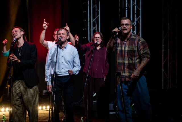 Grupa kilku osób na scenie przy mikrofonach