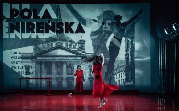 Dwie kobiety w czerwonych sukienkach na tle planszy z napisem POLA NIREŃSKA