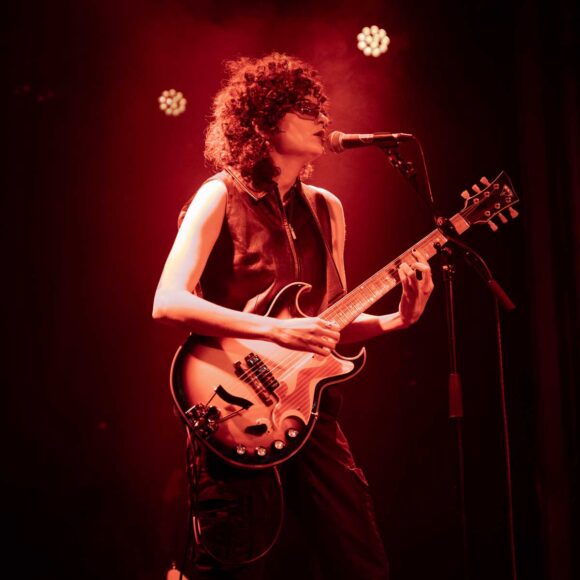 Kobieta z gitarą elektryczną przy mikrofonie w czerwonym świetle